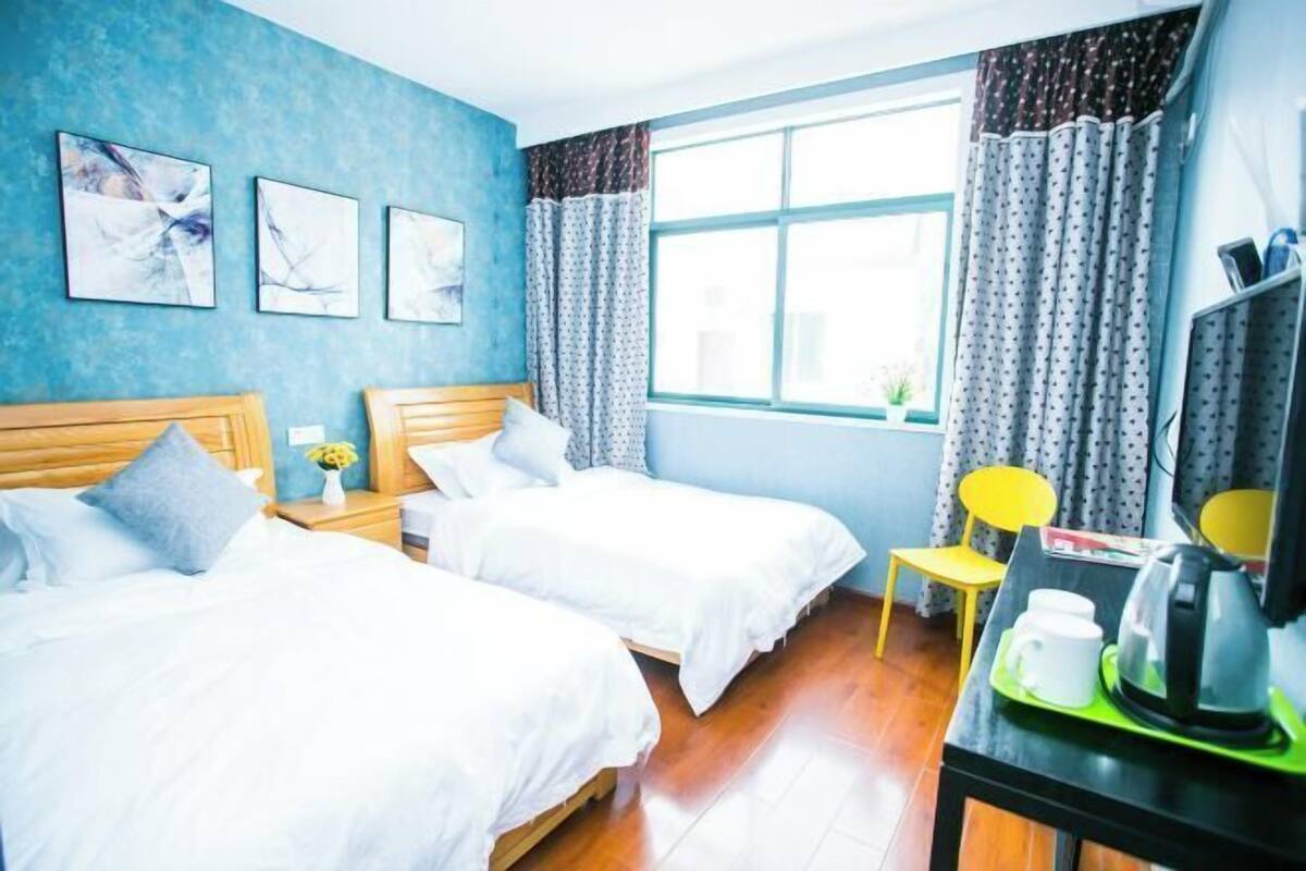 Una habitación con dos camas, una mesita con hervidor y una ventana con cortinas.