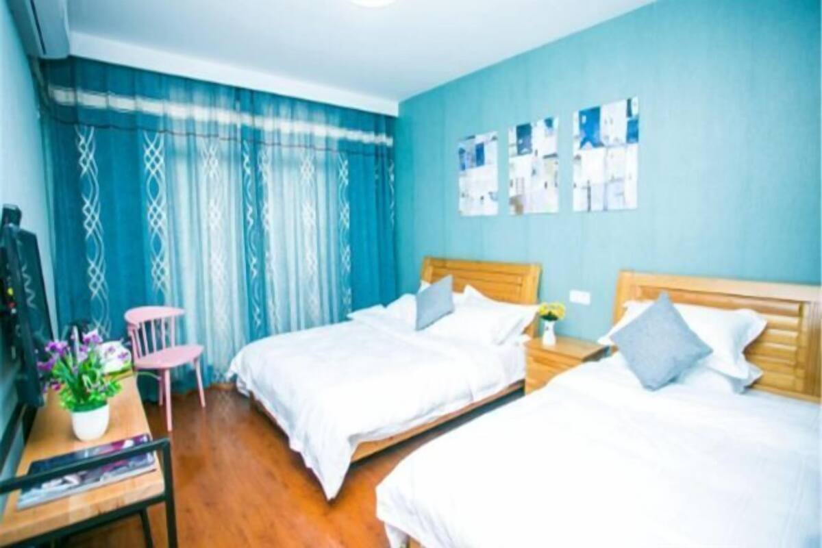 Habitación de hotel con dos camas, un escritorio con silla, televisión y ventana con cortinas.