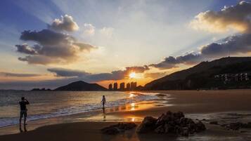 A beach scene with a sunset, a person taking a photo, and a distant cityscape.
