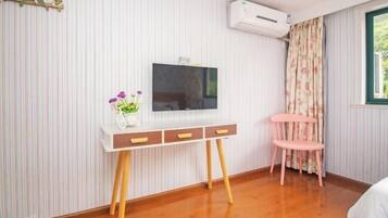 A room with a wooden floor, a white desk with drawers, a pink chair, a flat-screen TV, and a window with curtains.