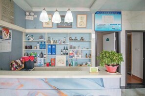 A reception area with a counter, shelves with various items, a potted plant, and a door leading to another room. - Lizhou Mountain Villa (Shengsi)