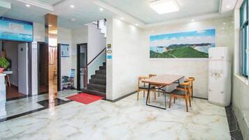 A hotel lobby with a marble floor, a staircase, a dining area with a table and chairs, and a refrigerator.