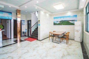 Un vestíbulo de hotel con piso de mármol, una escalera, una zona de comedor con una mesa y sillas, y un refrigerador.