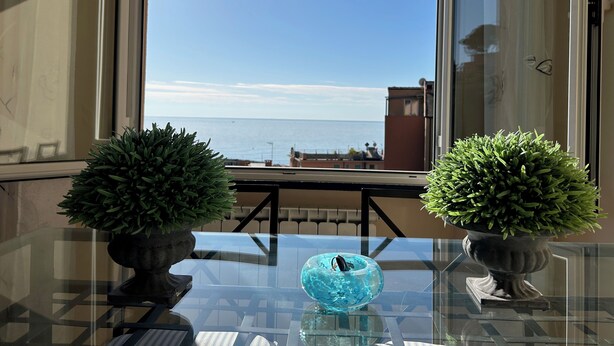 Ein Balkon mit einem Glastisch, zwei Kübelpflanzen und einer blauen Glasschale.