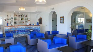 Een moderne lounge met blauwe en grijze zitmogelijkheden, een bar met een mozaïekachtergrond en een grote spiegel.