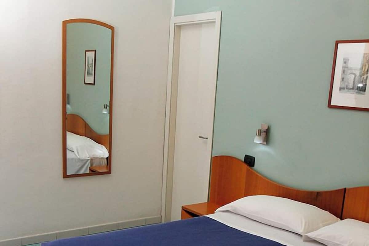 A bedroom with a bed, a nightstand, a mirror, and a door.