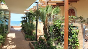 Een overdekte doorgang met uitzicht op zee, omgeven door weelderige begroeiing en een houten pergola.