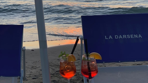 Een tafeltje aan het strand met drankjes en eten, met uitzicht op de oceaan bij zonsondergang.