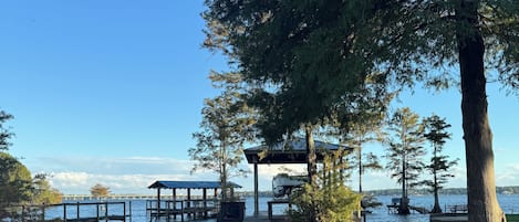 A wooden pier extending into calm water, surrounded by trees and a gazebo.