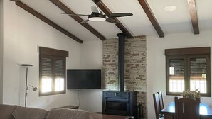 Una sala de estar con un sofá, un televisor montado en la pared, una chimenea y un comedor con sillas.