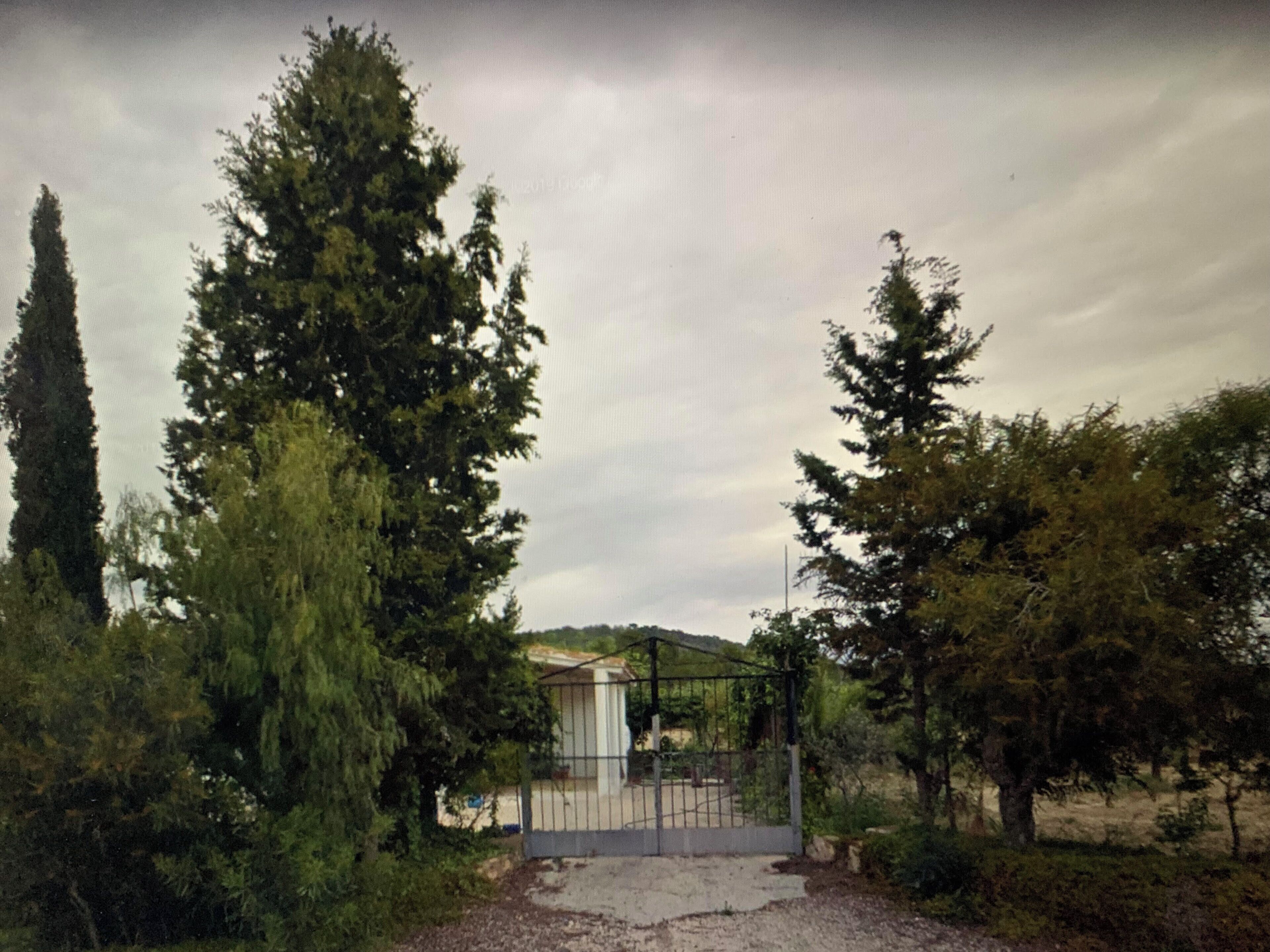 Un área resguardada por una cerca, con un edificio al fondo y rodeada de árboles altos.