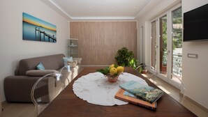 A modern living room with a sofa, a dining table with a white tablecloth, a fruit bowl, and books.