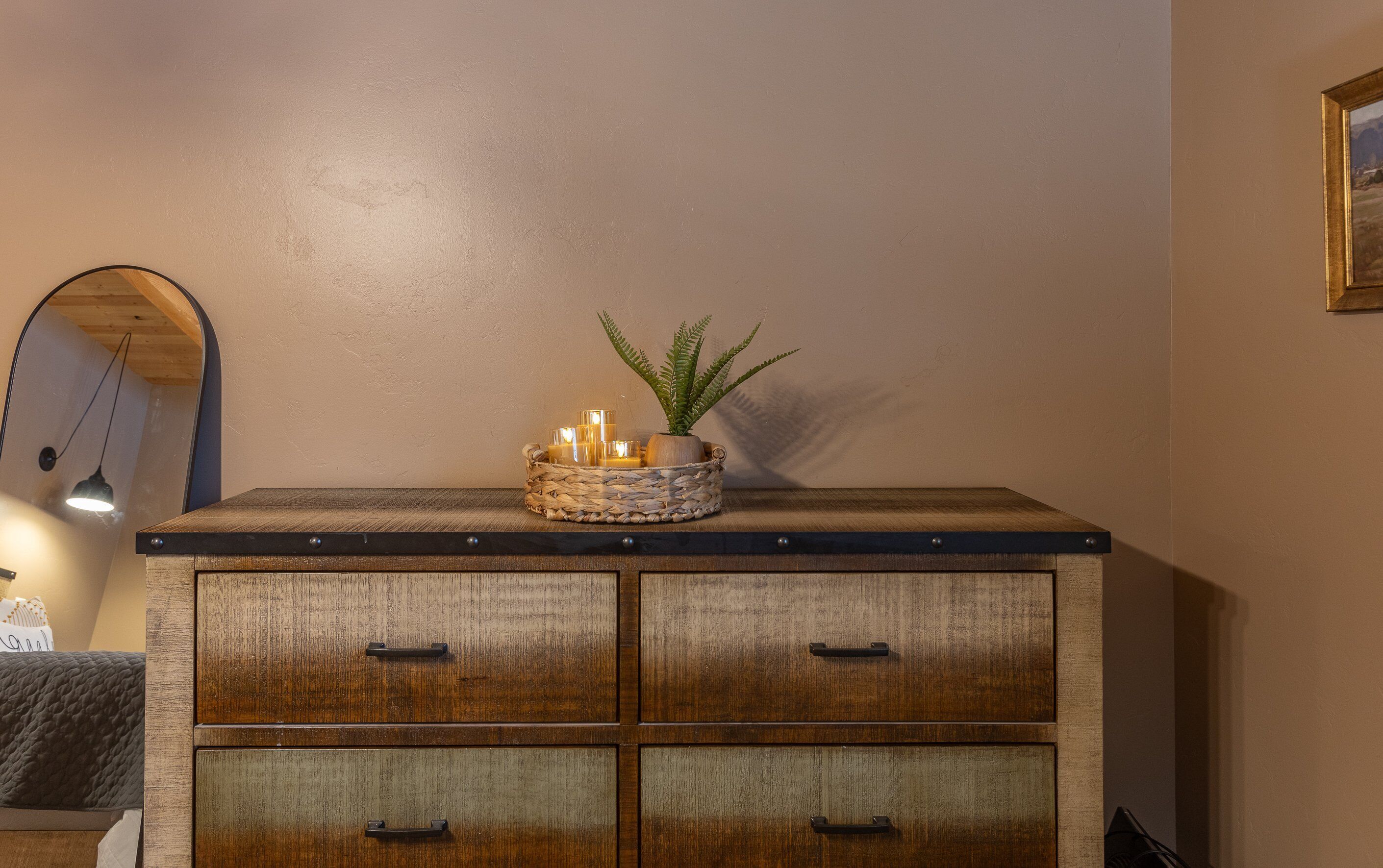 A wooden dresser with four drawers and a woven basket on top containing candles and a plant.