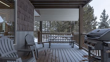 Relax on the deck with Adirondack chairs and a bench, surrounded by trees.