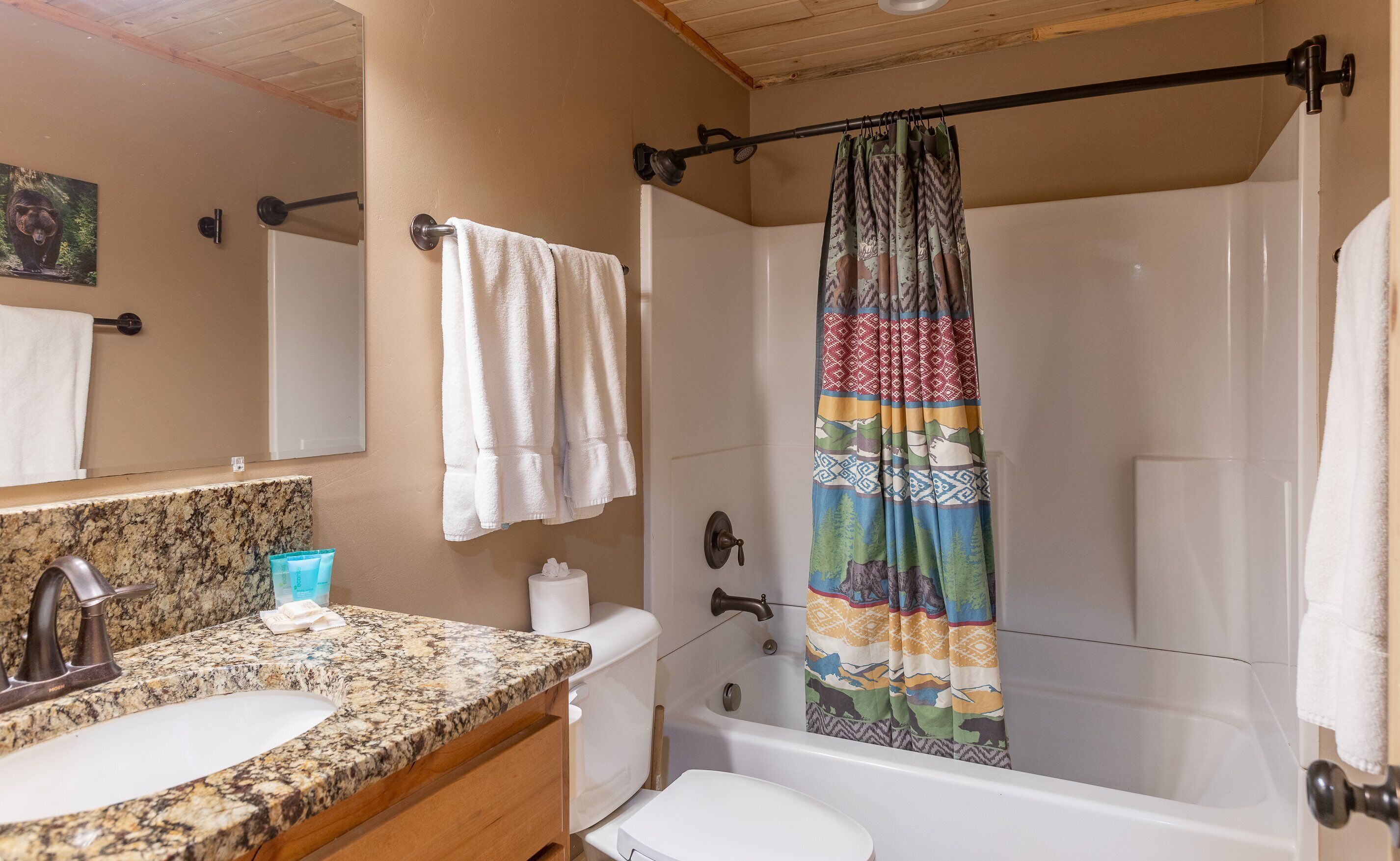Un baño con encimera de granito, lavamanos blanco y cortina de ducha con estampado colorido.