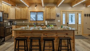 Una cocina con armarios de madera, encimera de granito, una isla central con taburetes, electrodomésticos de acero inoxidable y una ventana con persianas.