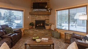 Una sala de estar acogedora con chimenea de piedra, sofás de cuero y ventanas amplias.