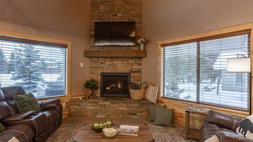 Relax by the fireplace in this inviting living room with a comfortable sofa and large windows offering a view of the outside.