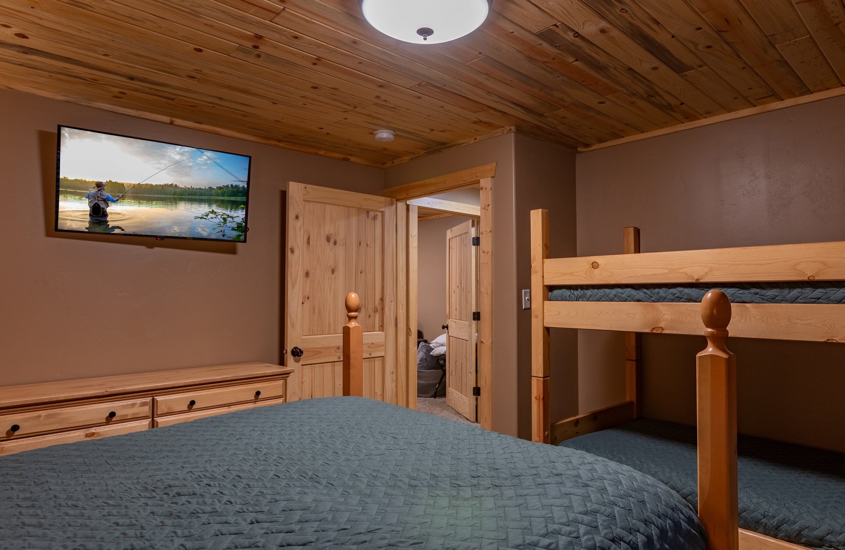 A room with a bunk bed, wooden ceiling, and a television displaying a fishing scene.