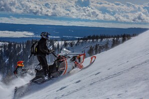 Uno scooter della neve su un pendio innevato, cielo sereno e montagne in lontananza.