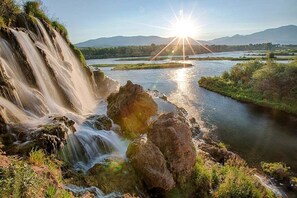 Una cascata che si getta su rocce in un fiume, con il sole al tramonto sullo sfondo.