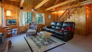 Een houten chalet van binnen met een leren bank, fauteuil en een televisie op een standaard.