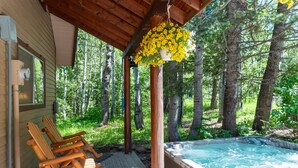 Een houten terras met Adirondack-stoelen, een jacuzzi en een bloemenmand.