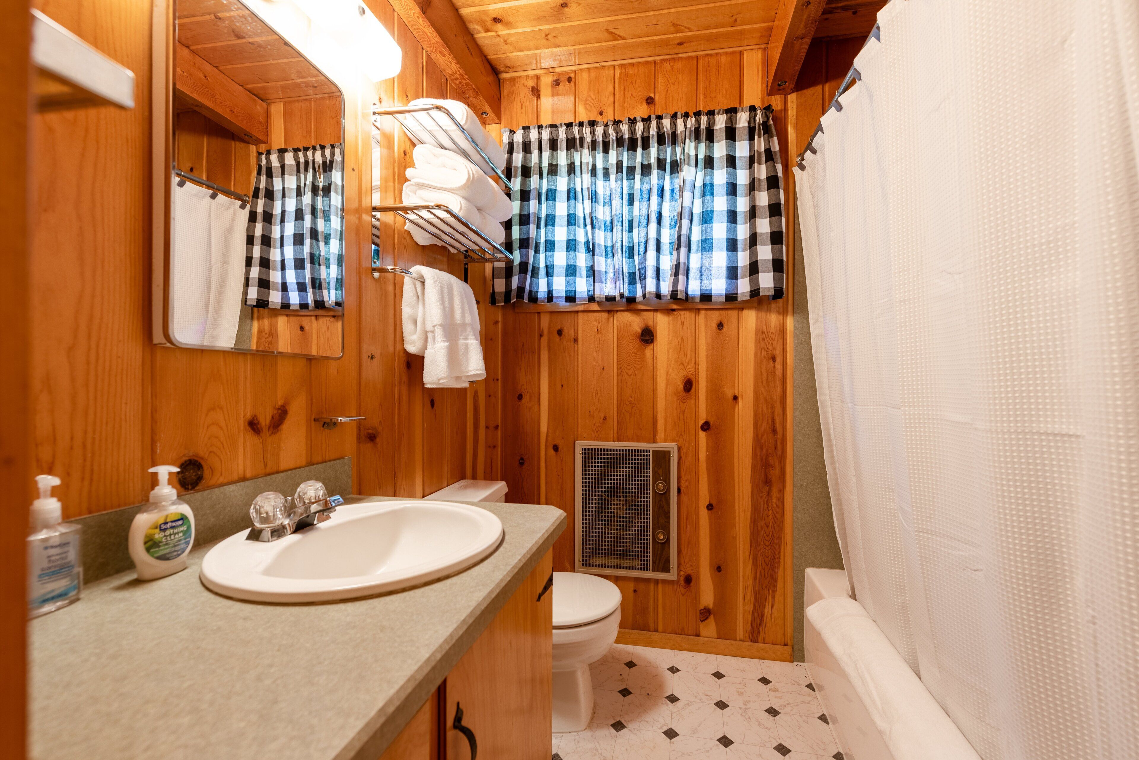 A wooden bathroom with a sink, toilet, and shower curtain.