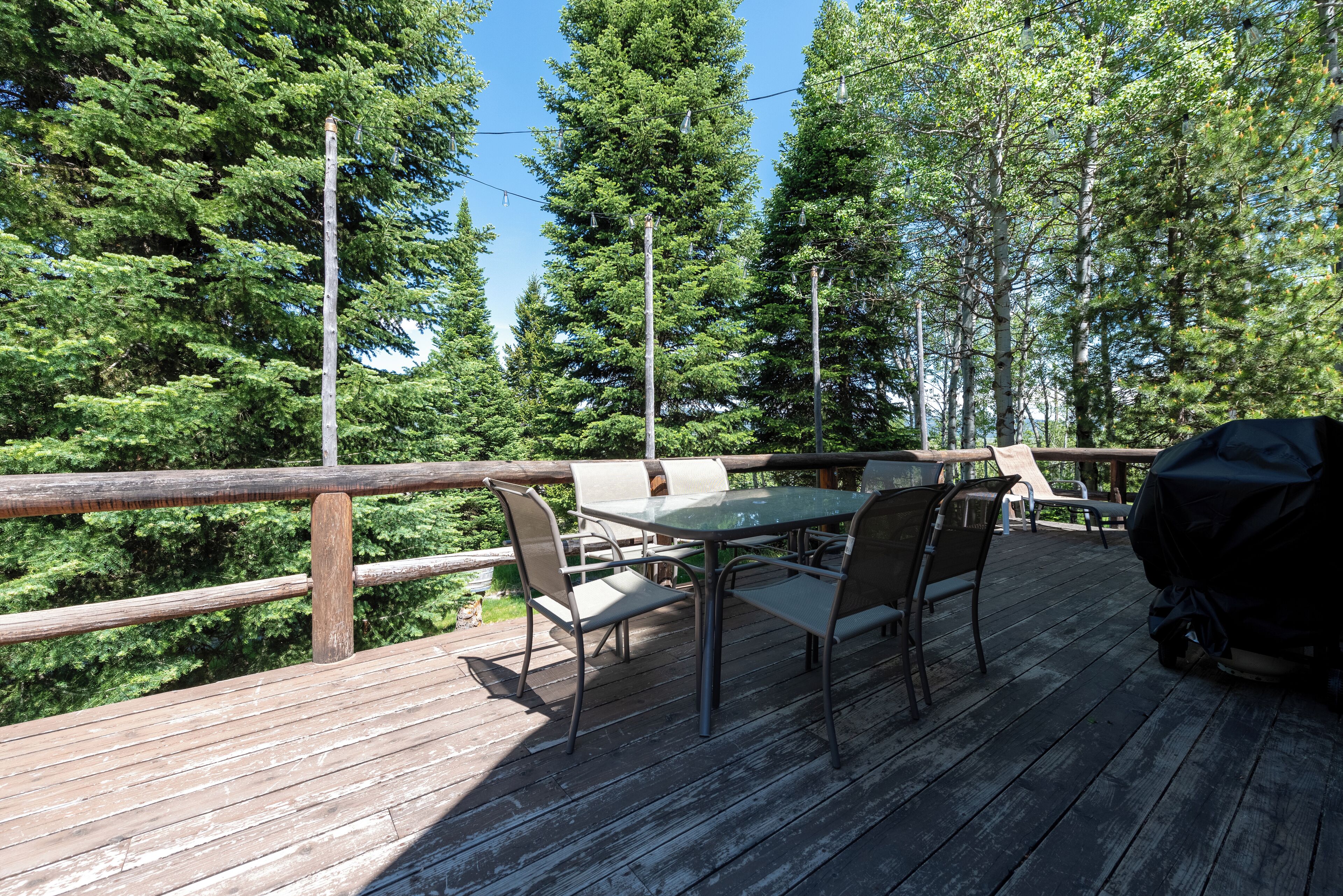 Une terrasse en bois avec une table et des chaises, entourée de grands arbres.