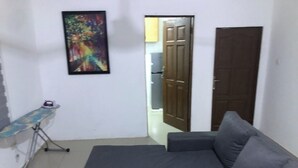 Una habitación con un sofá seccional gris, una pequeña mesa de madera, una tabla de planchar y un cuadro abstracto y colorido en la pared.