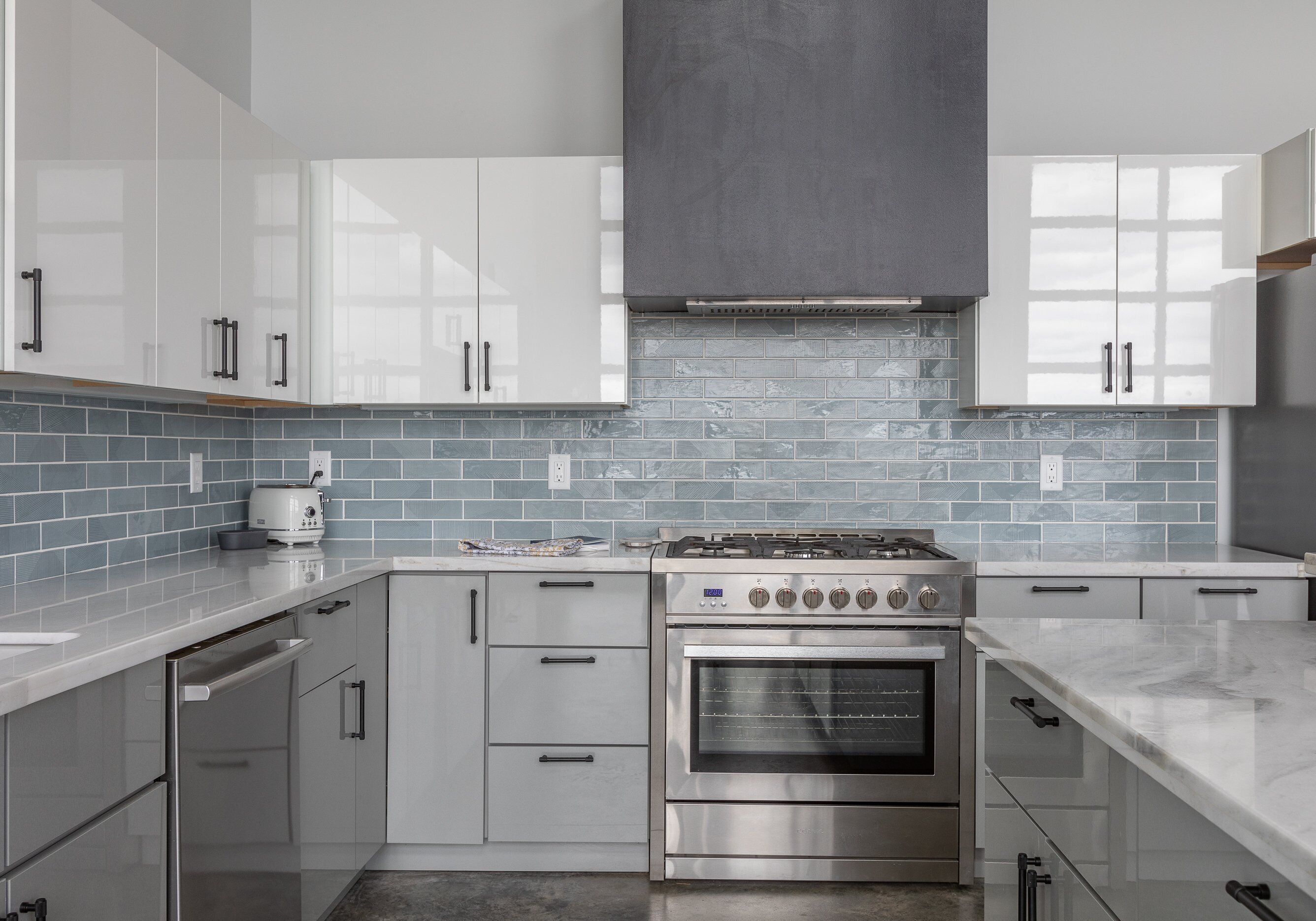 Une cuisine moderne dotée d’appareils électroménagers en acier inoxydable, de meubles blancs et d’un dosseret de carrelage bleu.