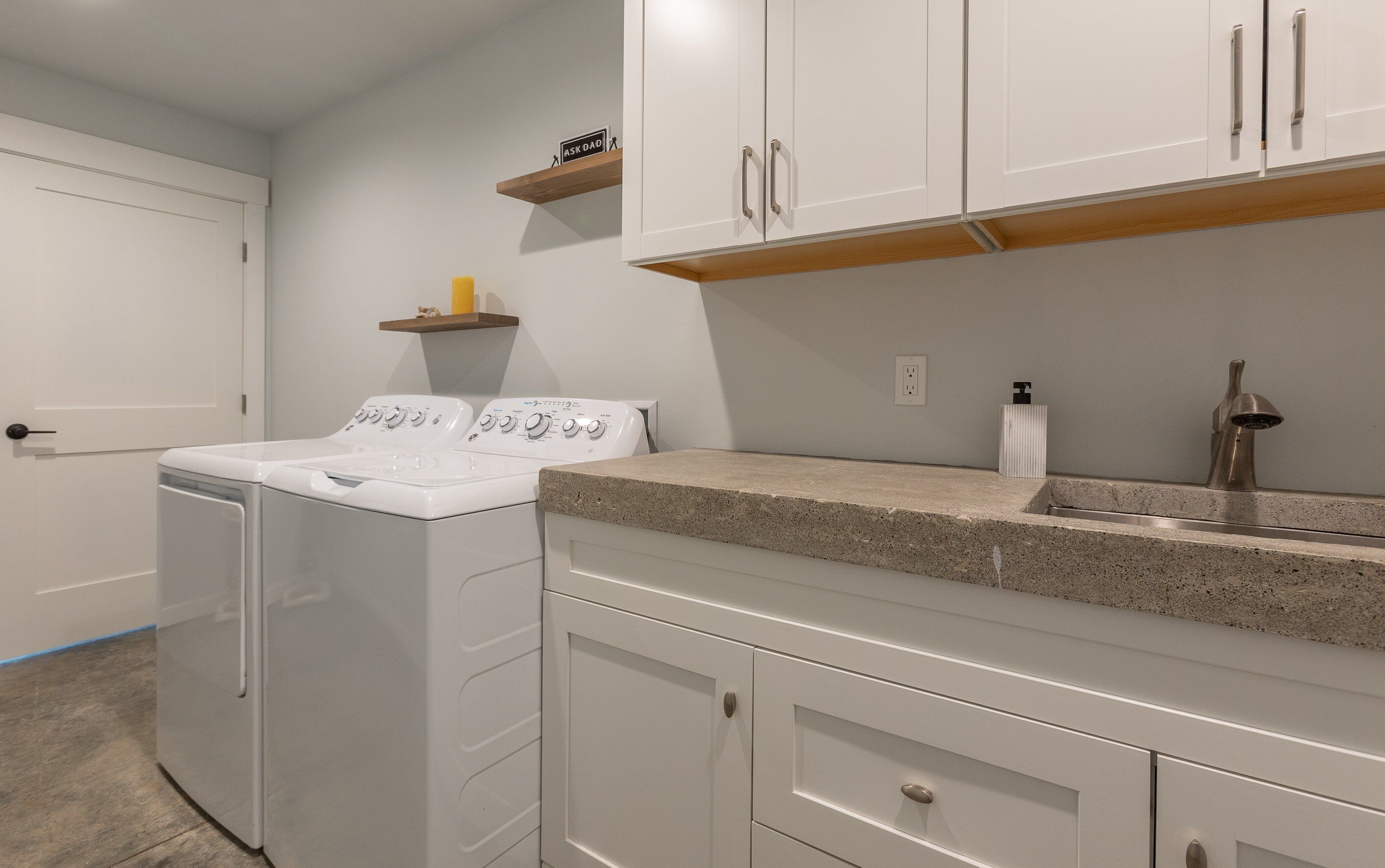 A laundry area with a washing machine and dryer, a countertop with a sink, and a shelf above the dryer.