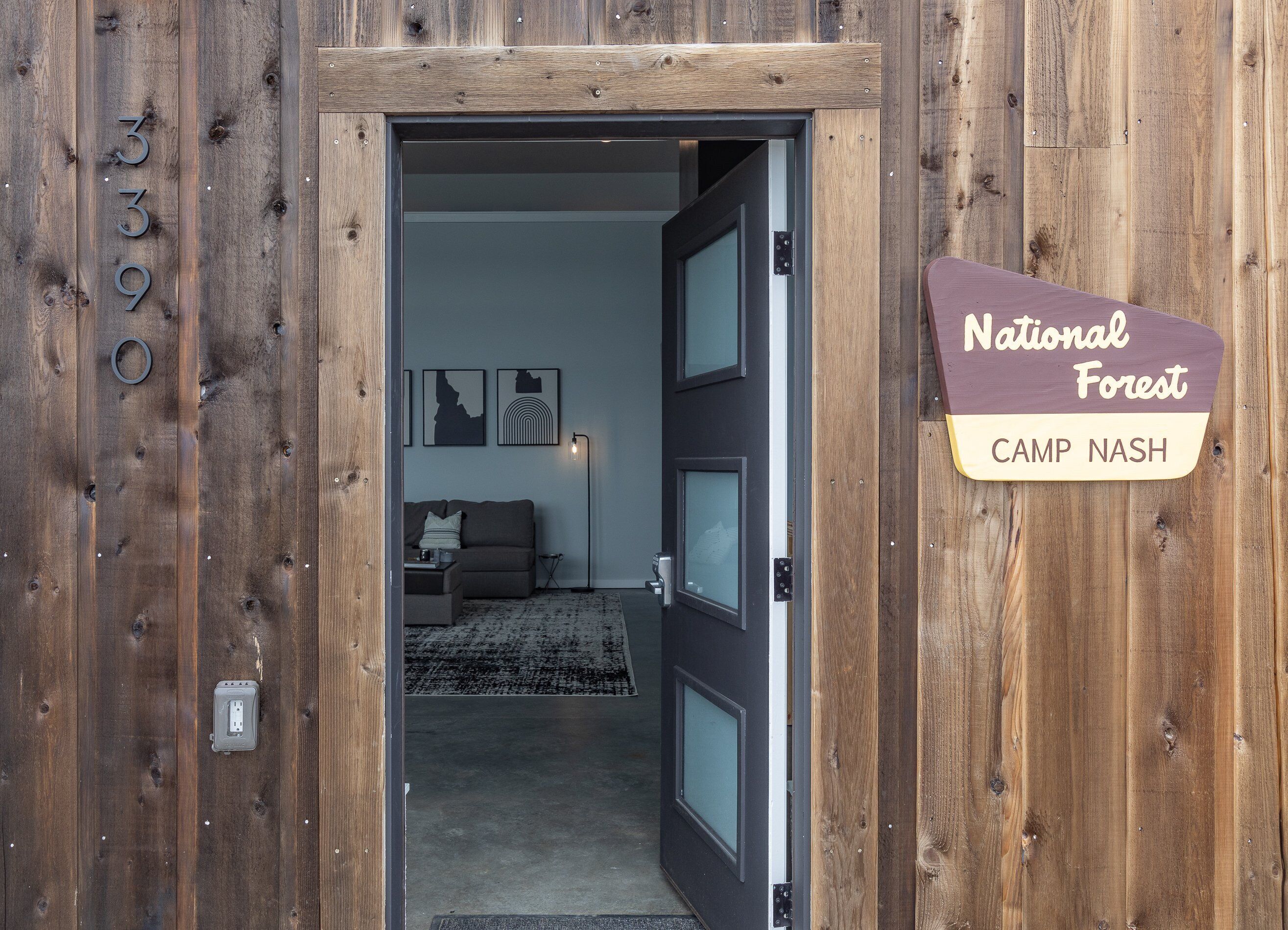 A wooden exterior with a door leading to an interior featuring a couch, a rug, and framed pictures on the wall.