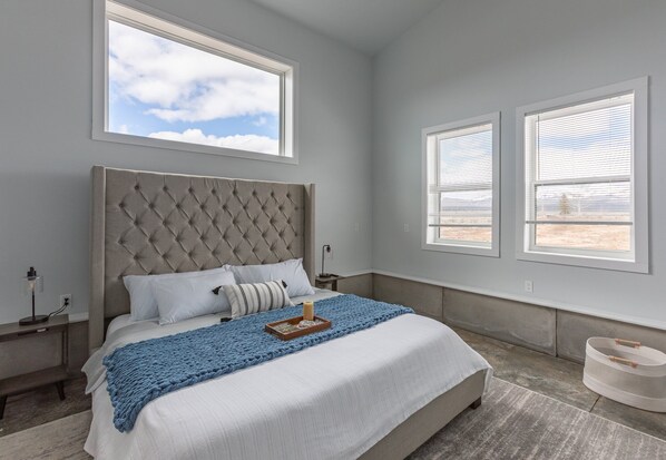A bedroom with a large bed, a window with blinds, a bedside table, and a nightstand. - Camp Nash (Island Park)