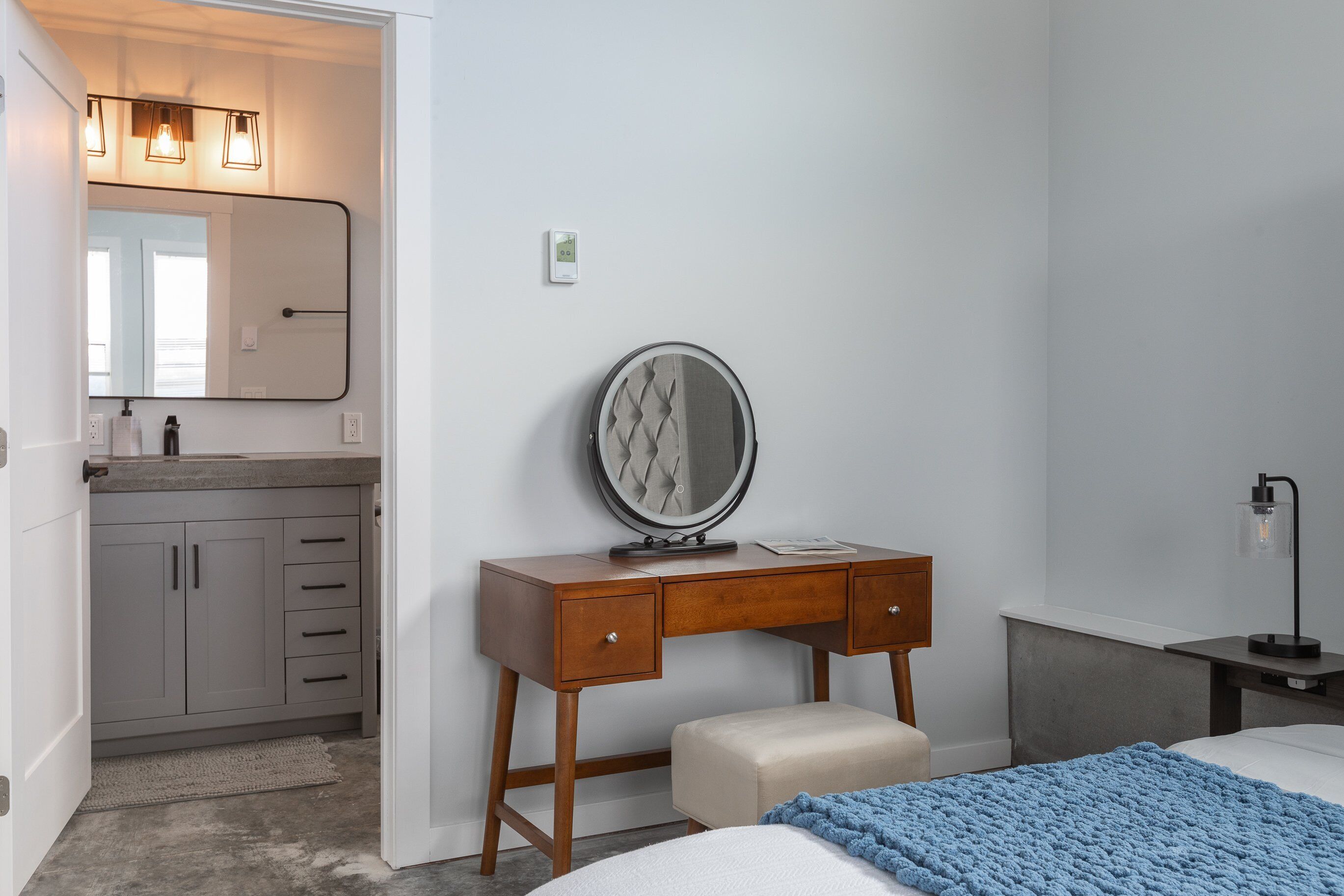 A bedroom with a bed, a bedside table, a nightstand, a dresser, a mirror, and a bathroom with a sink and mirror.