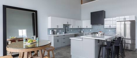 Eine moderne Küche mit weißen Schränken, einem Edelstahlkühlschrank und einem Glastisch mit Holzstühlen.