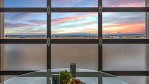 Uma mesa com um prato de comida e uma lata, vista através de uma janela com um pôr do sol.