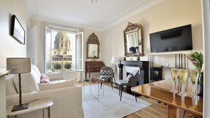 A modern living room with a sofa, armchairs, a fireplace, a TV, and a view of a historic building. - Charming Apartment w/ Iconic Views of Les Invalides (Paris)