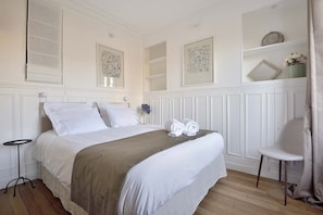 Ein ordentlich eingerichtetes Schlafzimmer mit einem Bett, Nachttischen und einem Sessel.