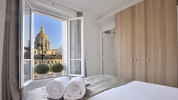 A bedroom with a large bed, a view of a historic building, and a wooden wardrobe. - Charming Apartment w/ Iconic Views of Les Invalides (Paris)