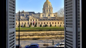 A view of a large, historic building with a prominent dome and classical architecture, viewed through open shutters. - Charming Apartment w/ Iconic Views of Les Invalides (Paris)