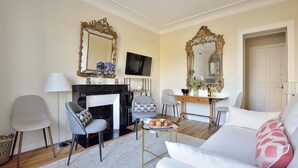 A living room with a fireplace, two armchairs, a sofa, a coffee table, and two ornate mirrors. - Charming Apartment w/ Iconic Views of Les Invalides (Paris)