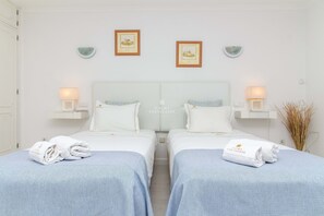 Une chambre d’hôtel avec deux lits, un grand lit avec une tête de lit, des tables de chevet avec des lampes et des œuvres d’art accrochées au mur.