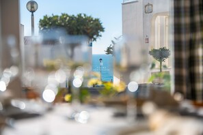 Une vue à travers une fenêtre, avec un ciel dégagé, un lampadaire et une enseigne indiquant « D. Alma Portuguesa ».