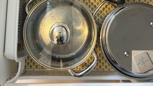 Eine Küchenschublade mit verschiedenen Kochutensilien, darunter eine Bratpfanne, ein Sieb, eine Reibe und zwei Töpfe mit Deckel.