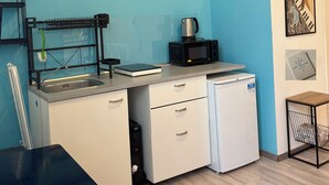Eine kompakte Küchenzeile mit Spüle, Mikrowelle und kleinem Kühlschrank. An den Wänden befinden sich gerahmte Kunstwerke, darunter eine Landschaftsmalerei vom Sonnenuntergang und eine Weltkarte.