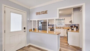 Een keuken met een houten eiland, witte kasten en een 'WELCOME' bord aan de muur.