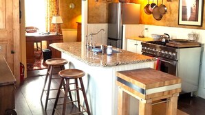 Een keuken met een centraal eiland, barstoelen, een fornuis en een hangende pannendroger.