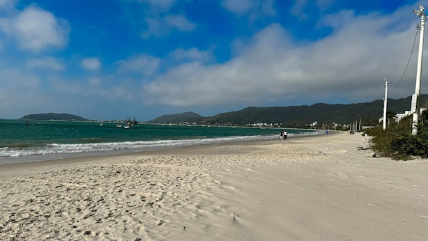 Ein Strand mit klarem, blauem Wasser, einem sandigen Ufer und einigen Spaziergängern.