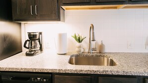 Una cocina con gabinetes de madera oscura, un lavamanos de acero inoxidable, una cafetera y una pequeña planta en la encimera.